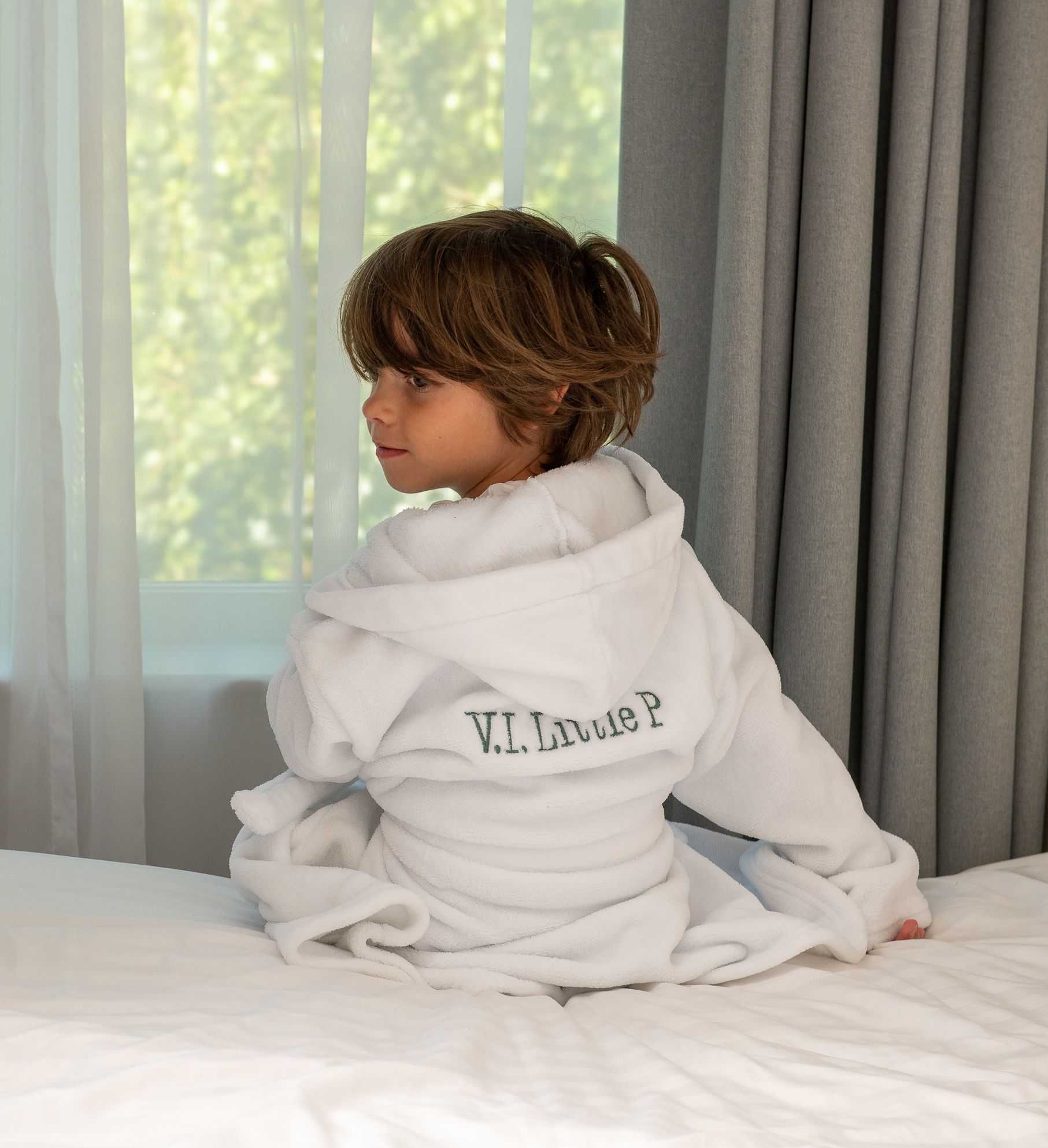 Child sitting on a hotel bed wearing a robe